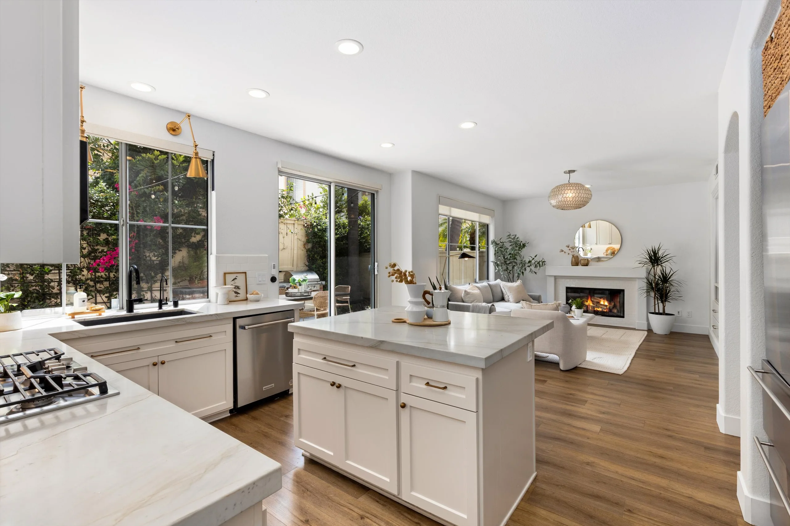 Open-concept kitchen at 5353 Renaissance Ave with quartzite island, stainless appliances and lit fireplace in the adjoining family room, listed by Kelli Miller, Encinitas Realtor | Compass