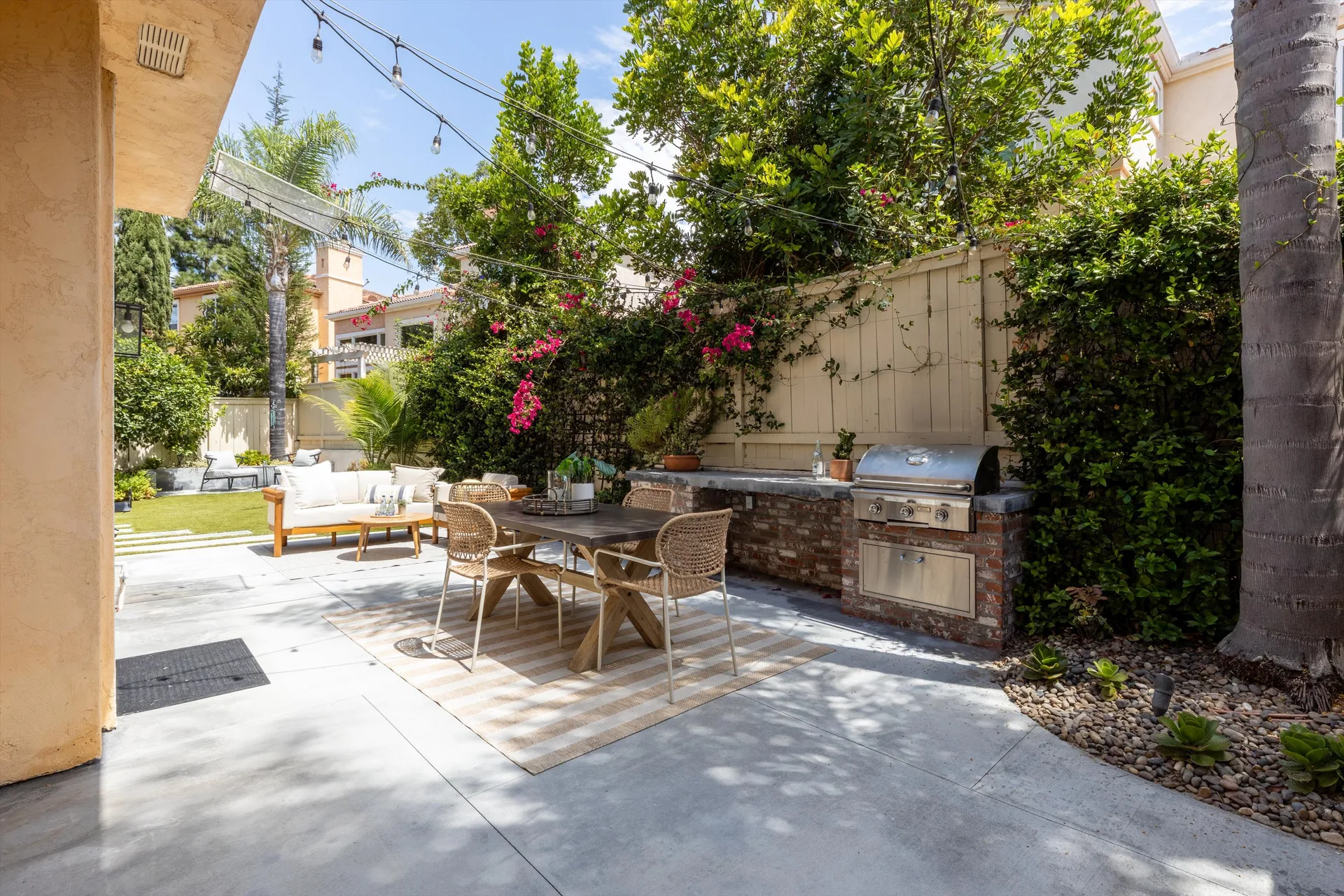 Private backyard patio with outdoor dining table, string lights and flowering bougainvillea at 5353 Renaissance Ave San Diego