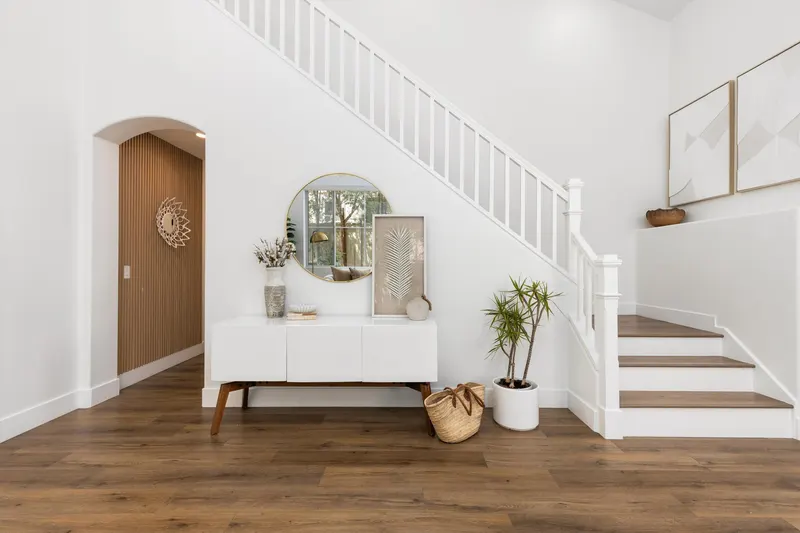 Entry foyer with white staircase, arched wood accent wall and round mirror at 5353 Renaissance Ave San Diego