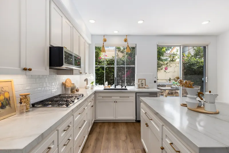 Kitchen with quartzite countertops, gas cooktop, white cabinetry and brass sconces at 5353 Renaissance Ave San Diego