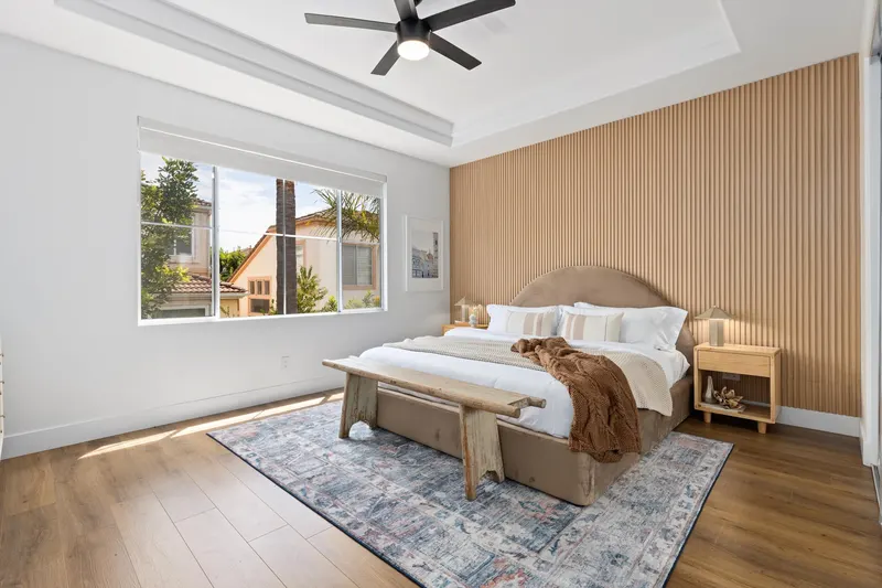 Primary bedroom with fluted wood accent wall, upholstered headboard and ceiling fan at 5353 Renaissance Ave San Diego