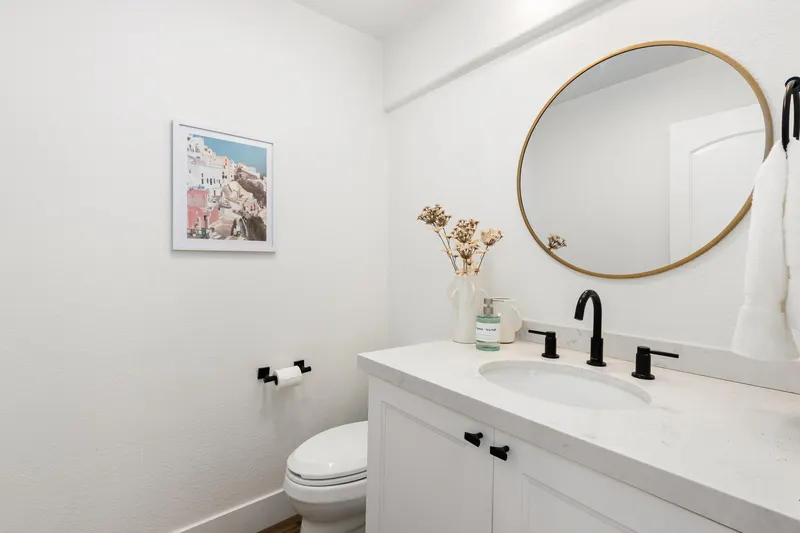 Powder bathroom with round brass mirror and matte black fixtures at 5353 Renaissance Ave San Diego