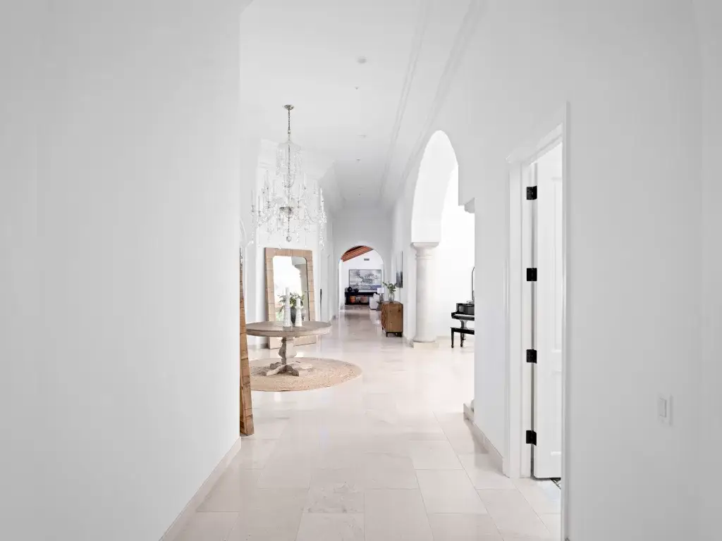 Grand interior gallery of a luxury North County San Diego estate featuring white arched transitions, limestone floors, and a crystal chandelier.