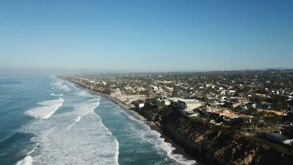 Aerial view of Encinitas coastline and Moonlight Beach looking north, featuring luxury oceanfront homes and Pacific Ocean waves under a clear blue sky.