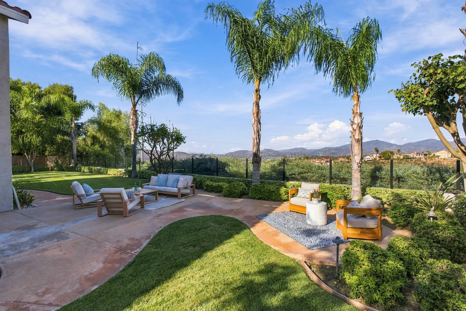 Backyard with concrete patio, two seating areas, lawn, palms and glass fencing open to canyon and mountain views at 12086 Little Silver Ct, Scripps Ranch, San Diego