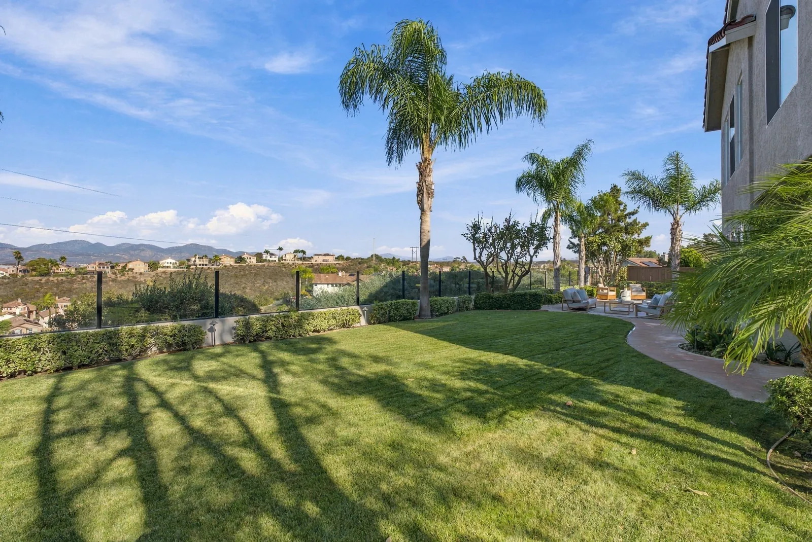 Main backyard lawn bordered by glass fencing with canyon and mountain views beyond at 12086 Little Silver Ct, Scripps Ranch, San Diego