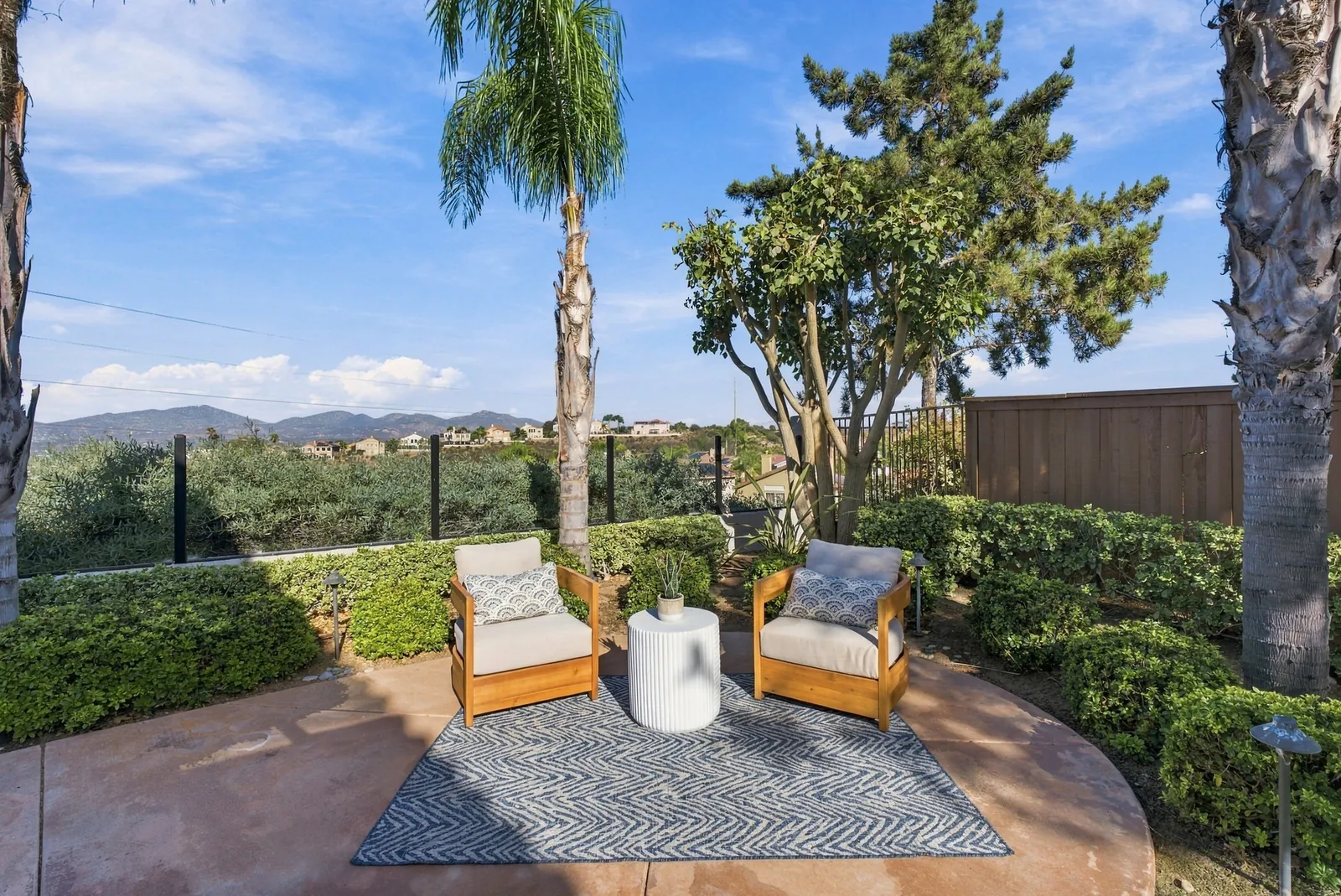 Two-chair seating nook at the edge of the patio framed by palms and hedges at 12086 Little Silver Ct, Scripps Ranch, San Diego