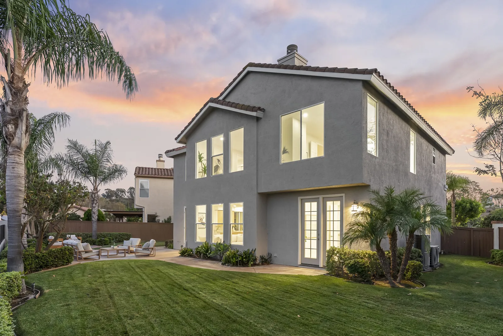 Rear of the home at twilight with lit windows, French doors to the patio and the main lawn at 12086 Little Silver Ct, Scripps Ranch, San Diego