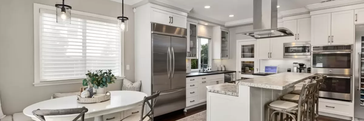 Gourmet kitchen at 11443 Bracken Fern Cove, San Diego. Features a granite center island with a Thermador cooktop and island hood, white cabinetry, built-in KitchenAid refrigerator, and sliding doors to the pool. Listed by Kelli Miller.